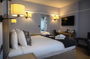 A hotel room with a large bed, bedside lamps, a desk with a chair, a TV, and a view of the hallway.