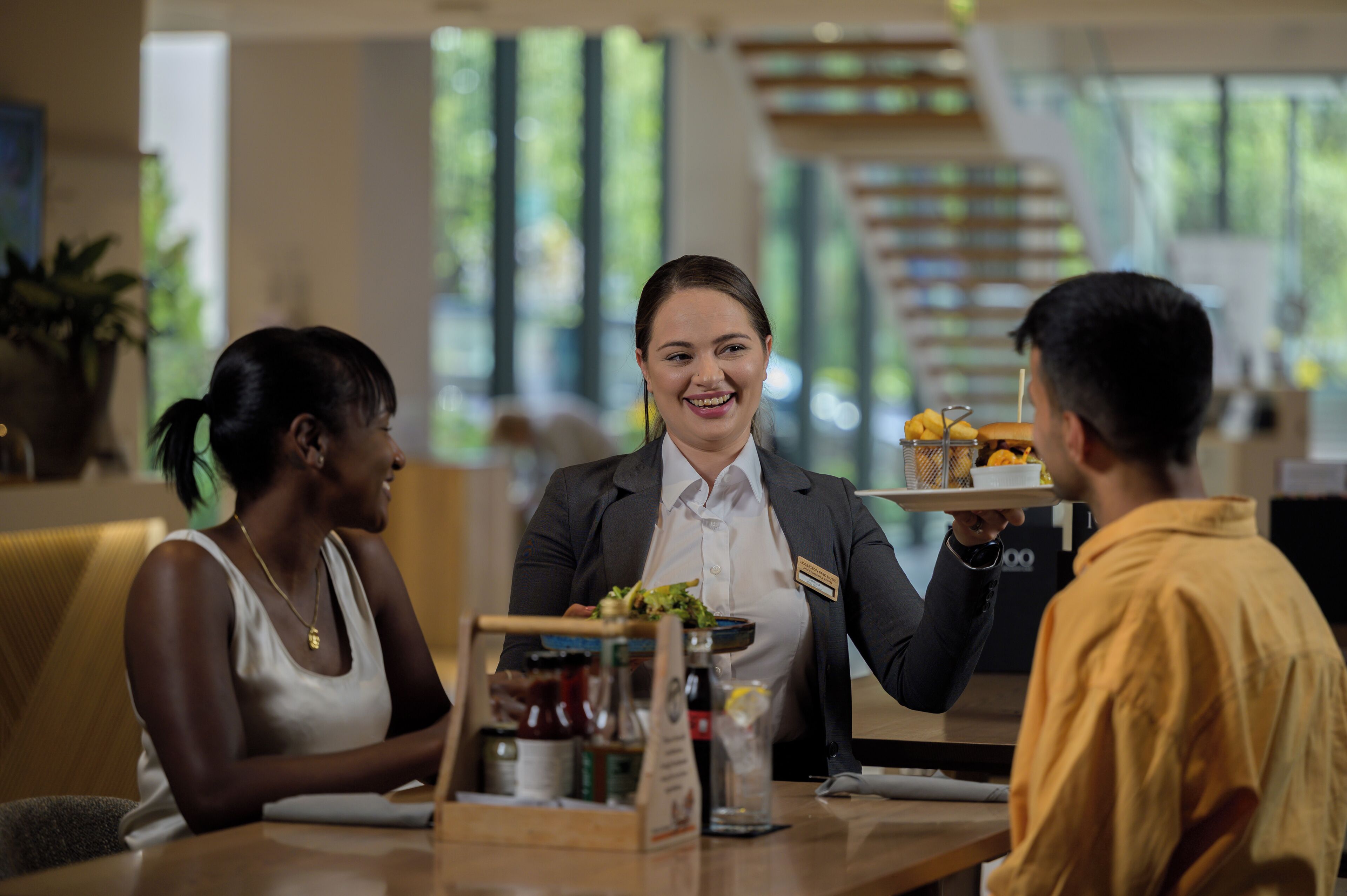 A restaurant setting with a waiter serving food to two guests.