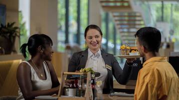 A restaurant setting with a waiter serving food to two guests.