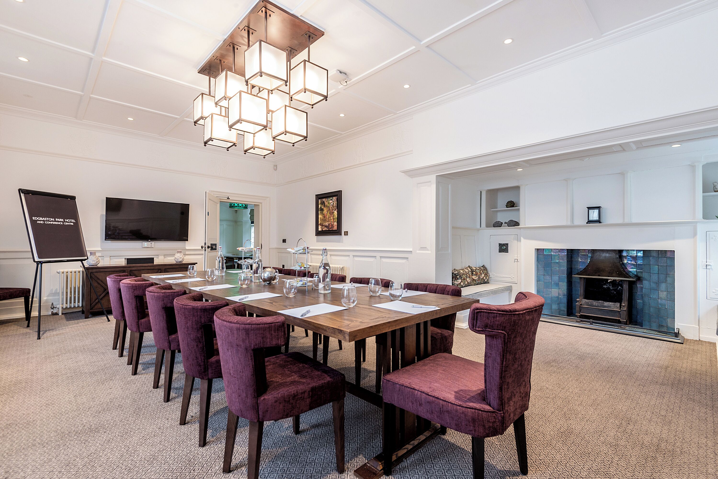 A conference room with a long table, purple chairs, a modern chandelier, a fireplace, and a television on the wall.