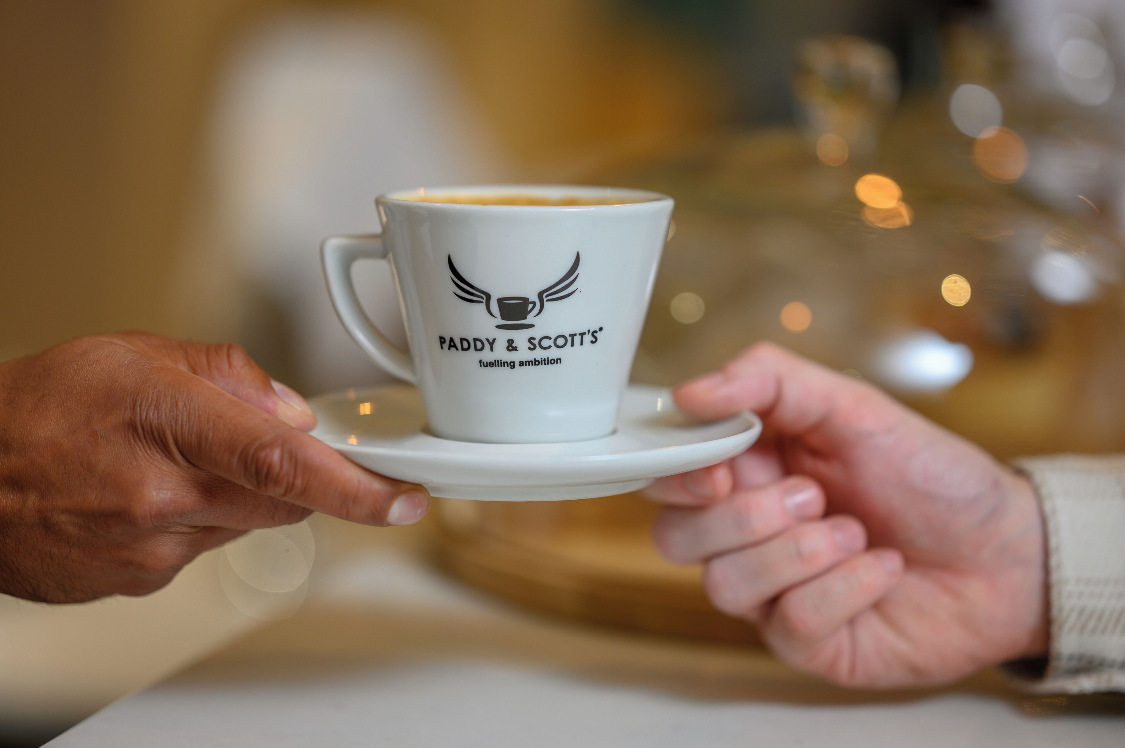 A cup with "Paddy & Scott's" logo and text "fueling ambition" on a saucer.