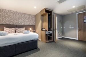 Ein modernes Hotelzimmer mit einem großen Bett, einem Schrank, einem Spiegel und einer Tür.
