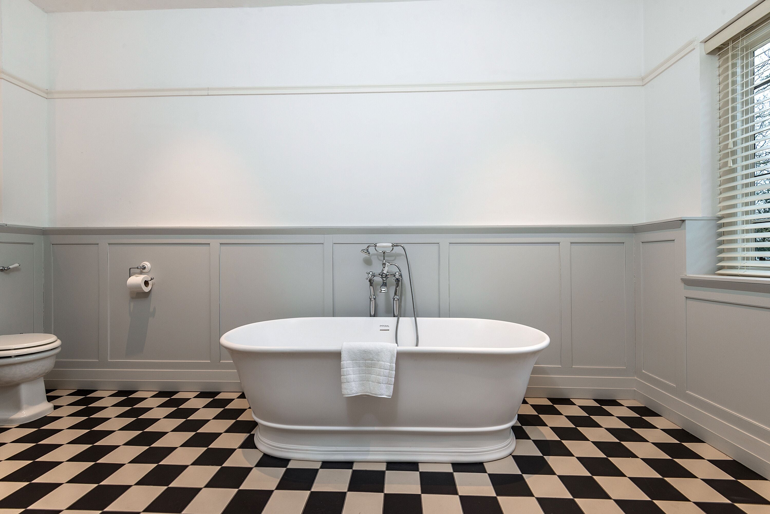 A bathroom with a freestanding bathtub, a toilet, and a checkered floor.