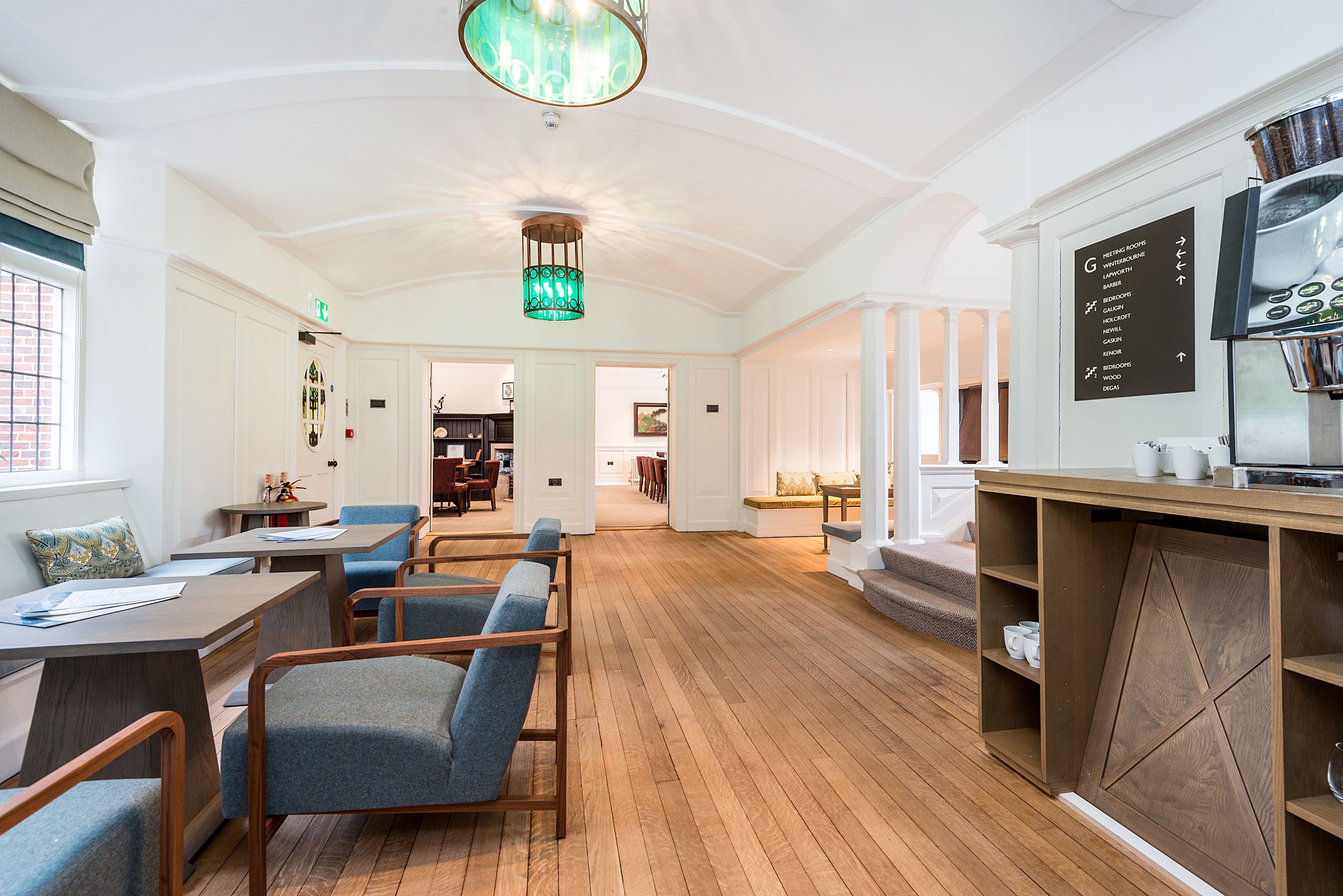 Une pièce spacieuse avec un plancher en bois, un coin repas avec des tables et des chaises, un coin cuisine équipé d’une cuisinière et d’un tableau noir servant de menu, et un escalier menant à un autre niveau.
