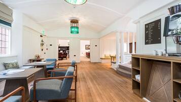A spacious room with wooden flooring, a dining area with tables and chairs, a kitchen area with a stove and a chalkboard menu, and a staircase leading to another level.
