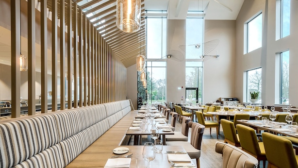 Un restaurante moderno con una larga mesa común, mesas individuales y un largo banco a lo largo de la pared.