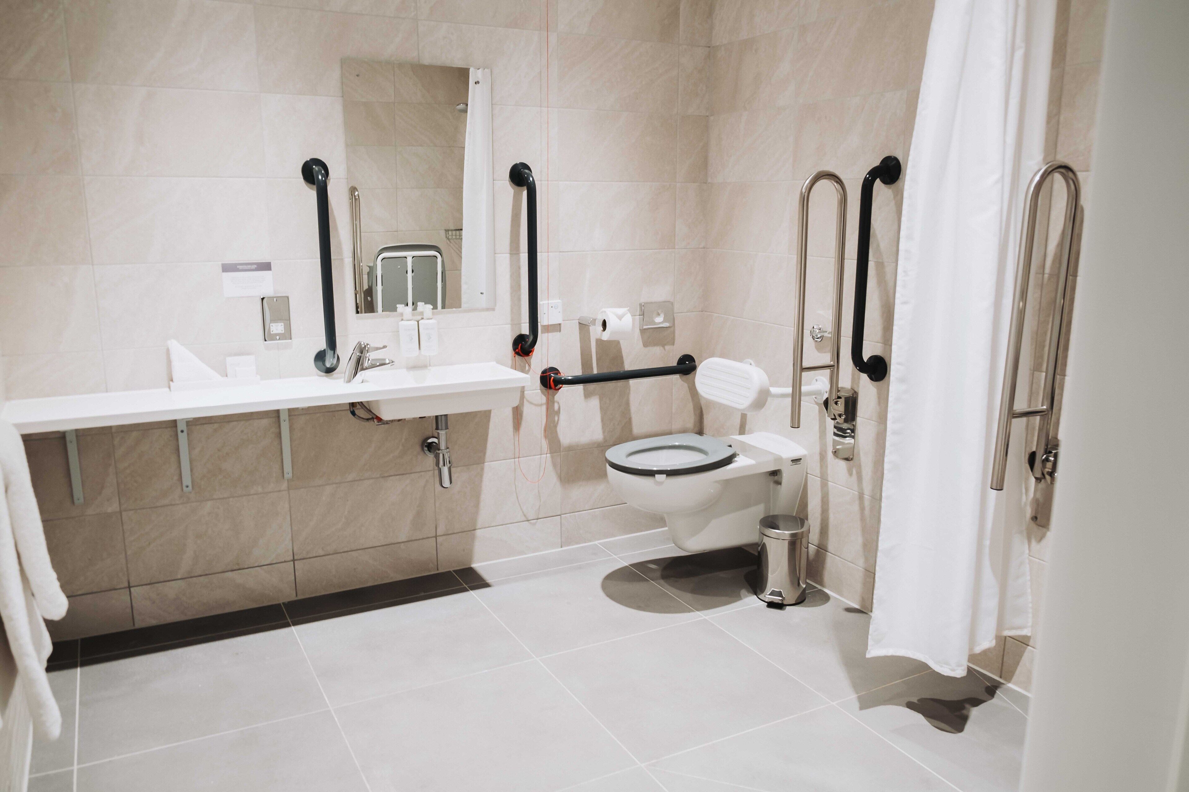 A modern bathroom with a toilet, sink, and handrails.