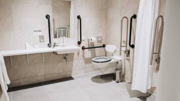 Un baño moderno con inodoro, lavamanos y barras de apoyo.