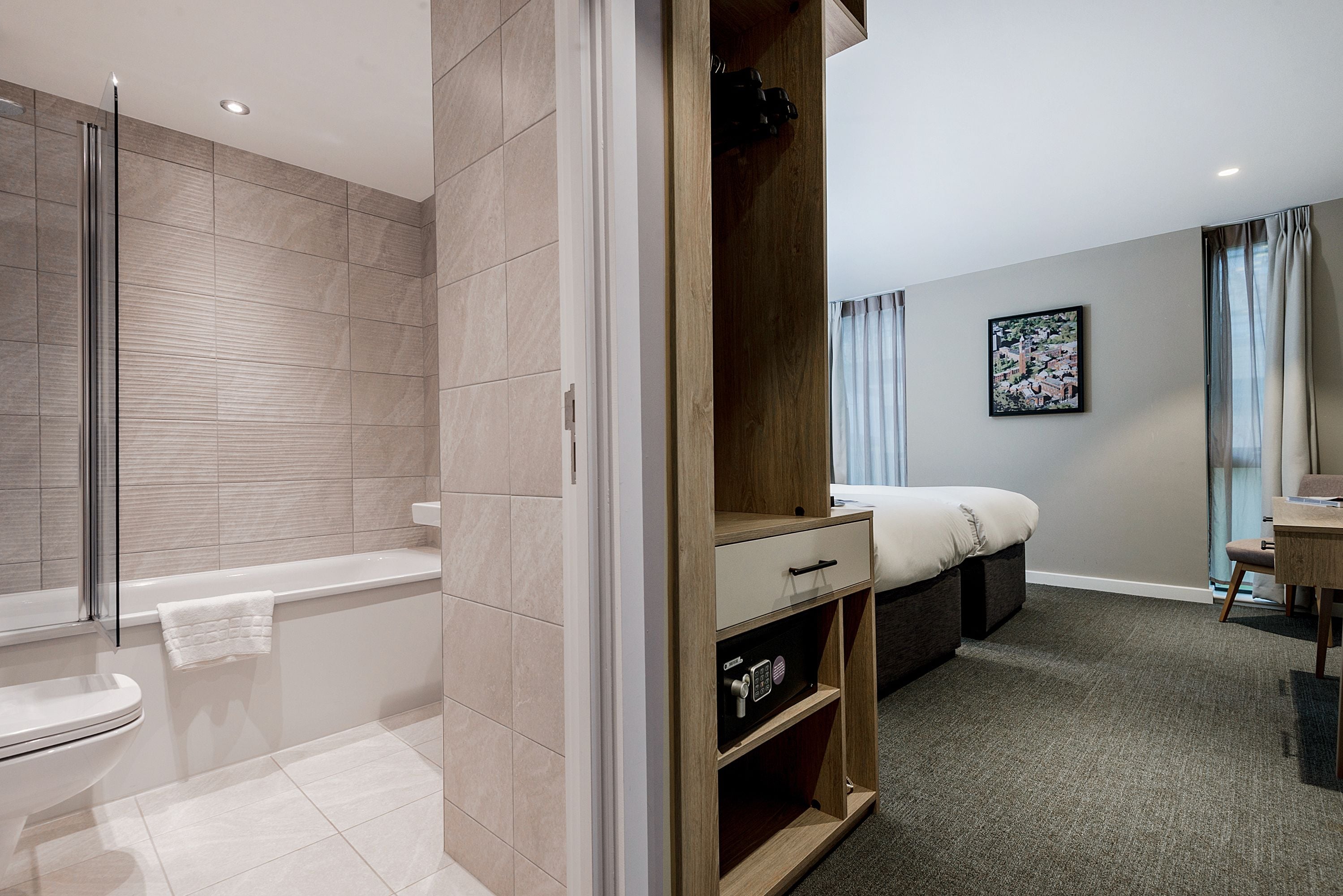 A modern bathroom with a bathtub, a shower, and a toilet. There is a wooden wardrobe with a drawer and shelves.