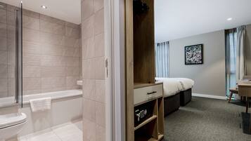 A modern bathroom with a bathtub, a shower, and a toilet. There is a wooden wardrobe with a drawer and shelves.