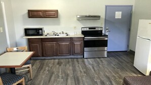 A compact kitchen with a microwave, stove, sink, and cabinets. - Jefferson Inn and Suites (Newport News)