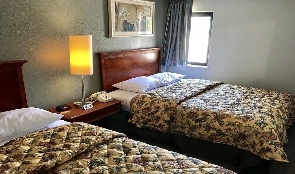 Habitación de hotel con dos camas, una mesita de noche con lámpara, teléfono y un cuadro en la pared.