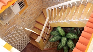 Eine Treppe mit Metallgeländer, eine Wand mit Steinmuster und eine Pflanze mit gemusterten Blättern.
