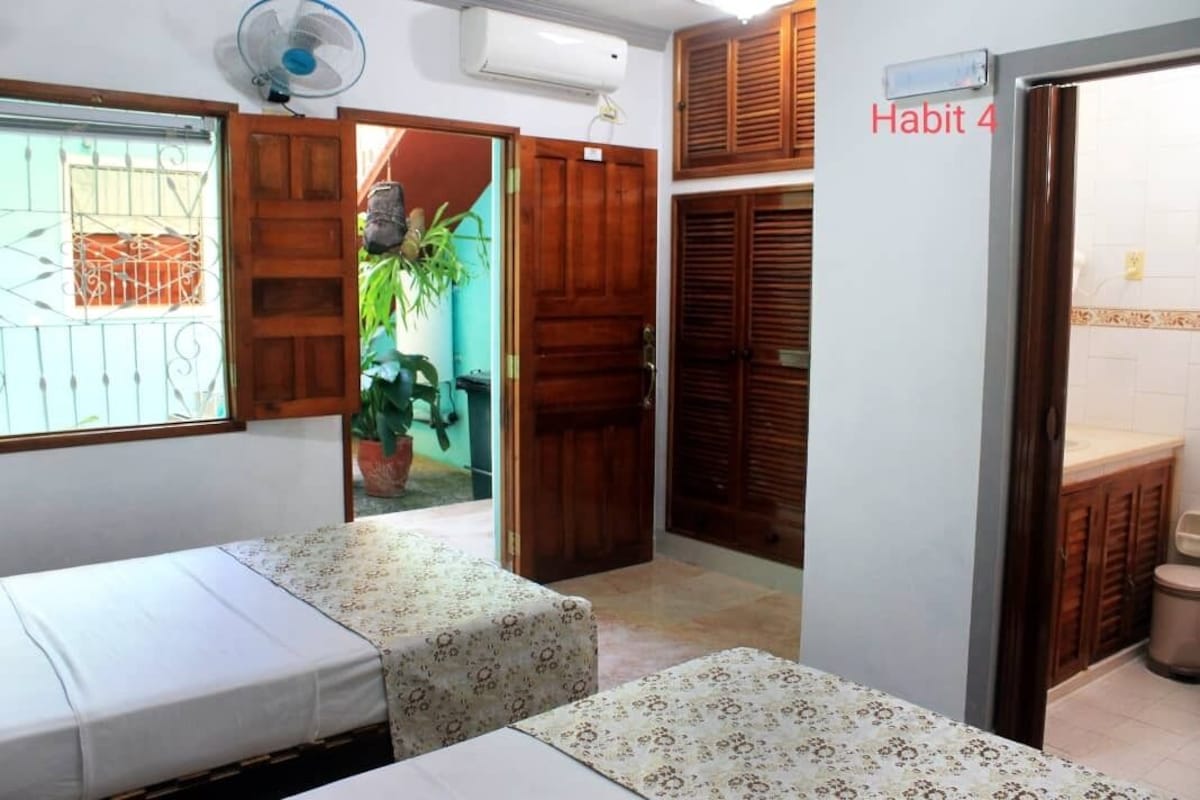 A room with two beds, wooden doors, a fan, and a sign reading "Habit 4".