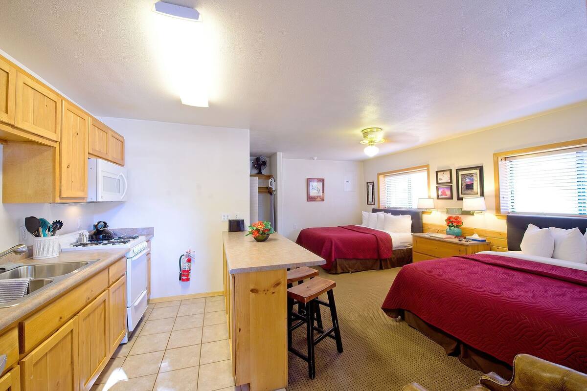 Quarto de hotel compacto com cozinha compacta, duas camas, um pequeno espaço para refeições e banheiro.