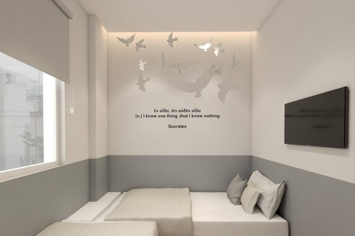 A modern bedroom with two beds, a wall-mounted TV, and a decorative wall with flying birds and a quote by Socrates.