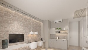 A modern kitchen with a stone wall, a flat-screen TV, pendant lights, a dining area with a round table and chairs, and a built-in microwave. - Great Living Koukaki (Athens)