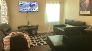 A living room with a black leather sofa, a television mounted on the wall, a patterned rug, and a framed picture on the wall. - Alleyne's Place (Hitchcock)