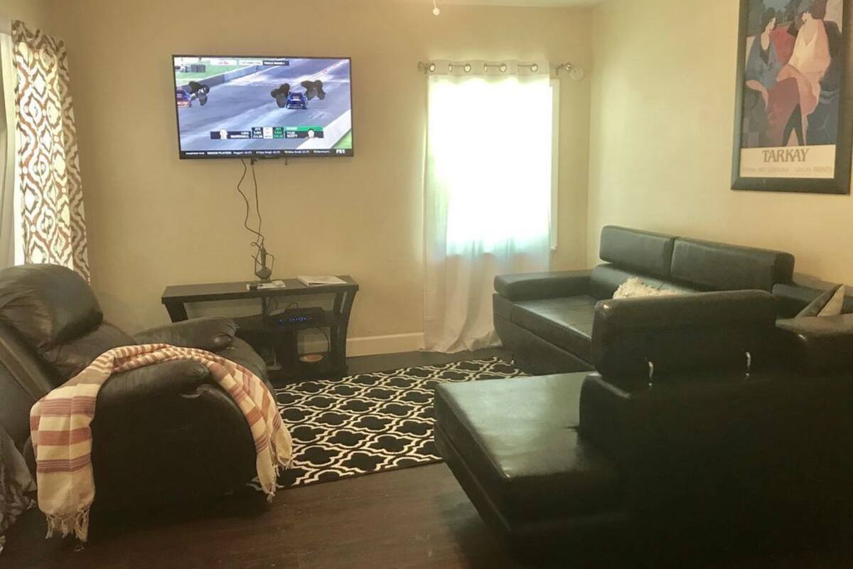 A living room with a black leather sofa, a television mounted on the wall, a patterned rug, and a framed picture on the wall.