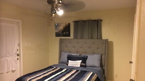 A bedroom with a bed, a ceiling fan, a painting, and curtains. - Alleyne's Place (Hitchcock)