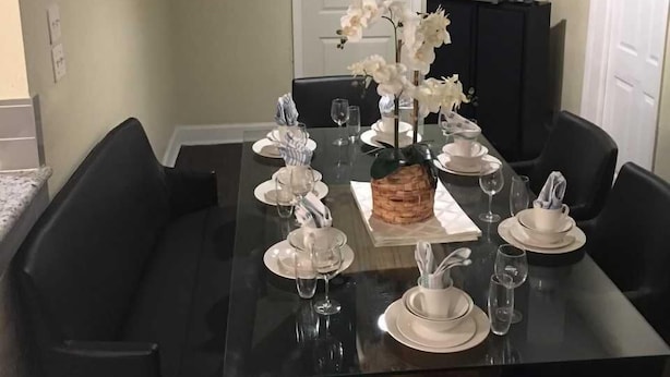A dining table set for six with white plates, glasses, and a centerpiece of white flowers. - Alleyne's Place (Hitchcock)