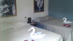 A hotel room with two beds, each with a swan-shaped towel and a flower on the bed. There are posters on the wall and a small table with a lamp. - El Jardín de Daynelis (Viñales)