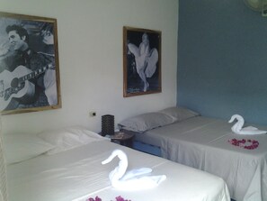 A hotel room with two beds, each with a swan-shaped towel and a flower on the bed. There are posters on the wall and a small table with a lamp. - El Jardín de Daynelis (Viñales)