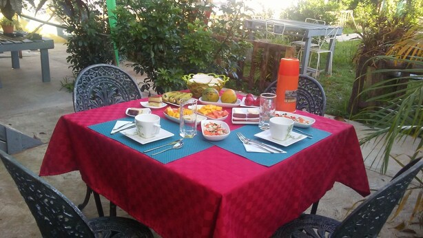 An outdoor dining area with a red tablecloth, various dishes, and drinks. - El Jardín de Daynelis (Viñales)