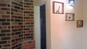 A hallway with a brick wall, a door, and three framed pictures on the wall. - El Jardín de Daynelis (Viñales)
