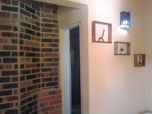 A hallway with a brick wall, a door, and three framed pictures on the wall. - El Jardín de Daynelis (Viñales)