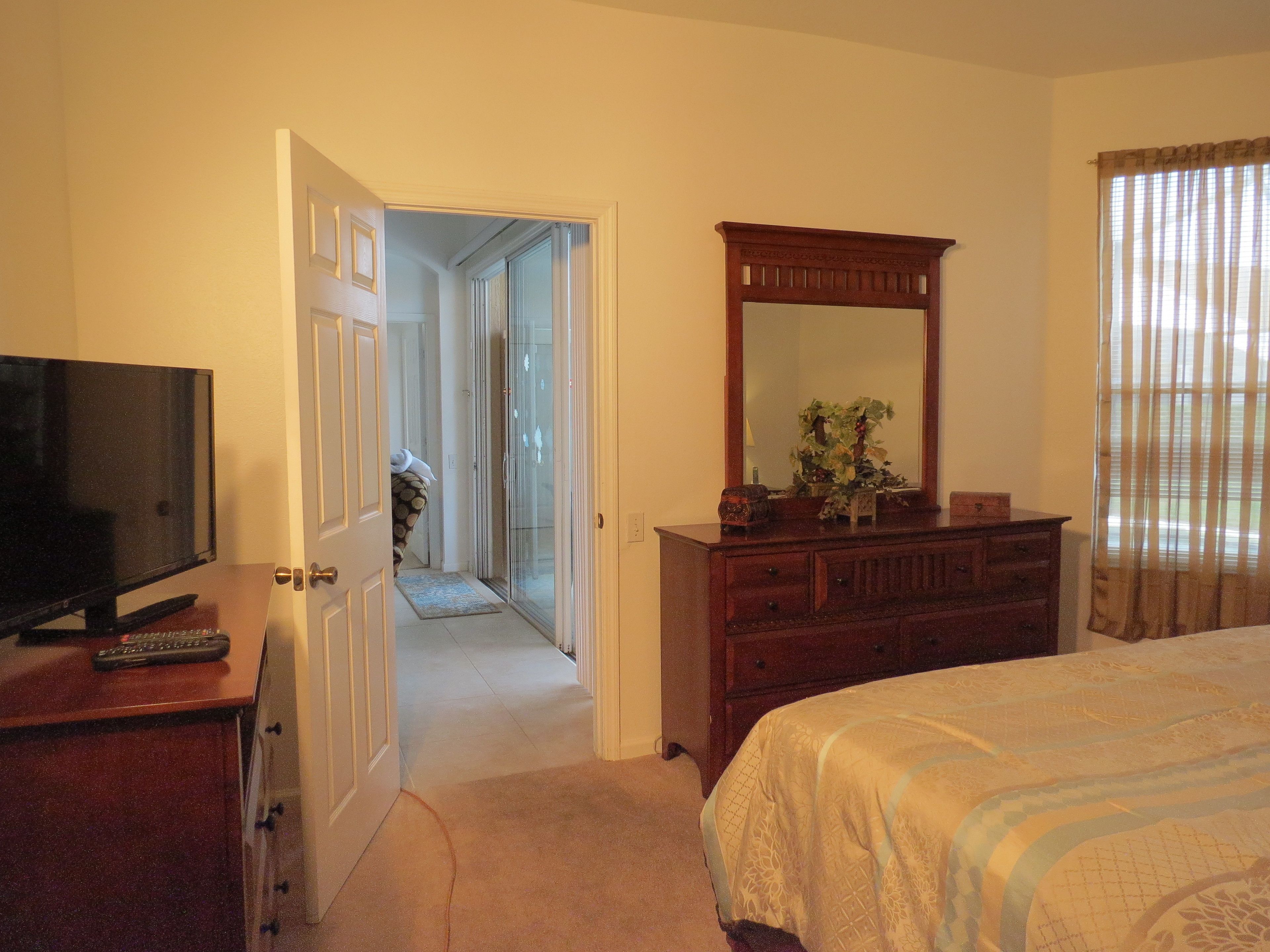 Une chambre d’hôtel comprenant un lit, une commode, un téléviseur et une porte donnant sur un couloir.