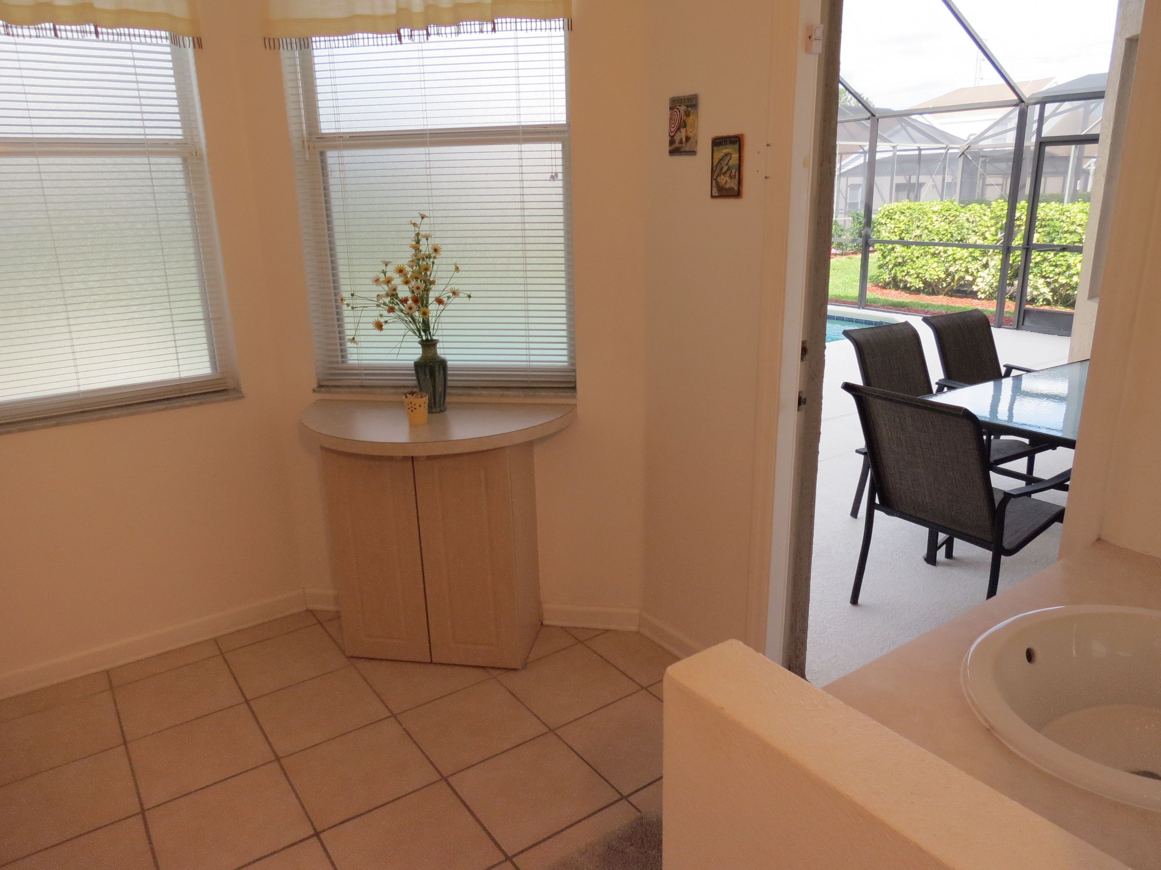 A bathroom with a sink, a small table with a vase, and a window with blinds.