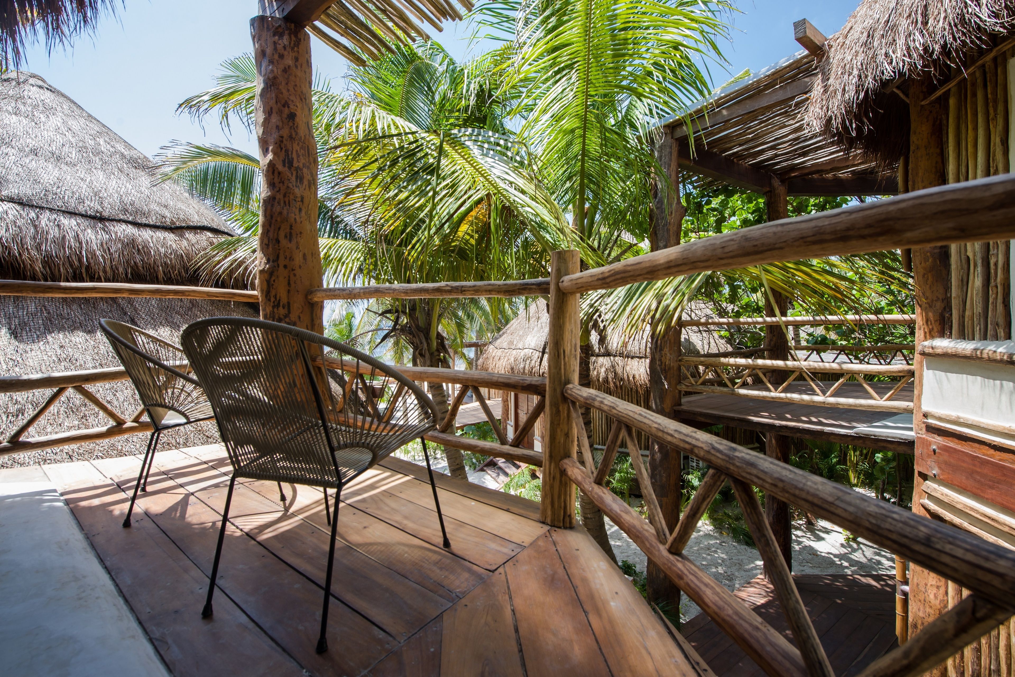 A wooden deck with a chair, surrounded by a wooden fence and palm trees.
