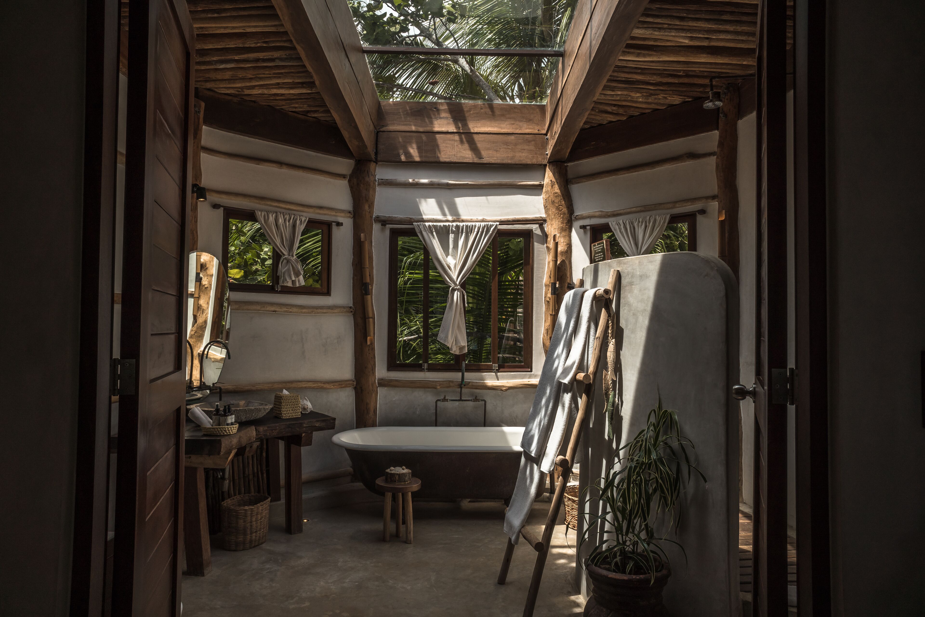 Une salle de bain avec une baignoire, un meuble-lavabo avec un miroir, un petit tabouret et une plante en pot.