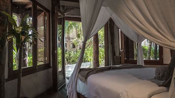A bedroom with a large bed, a potted plant, and a view of the outdoors.
