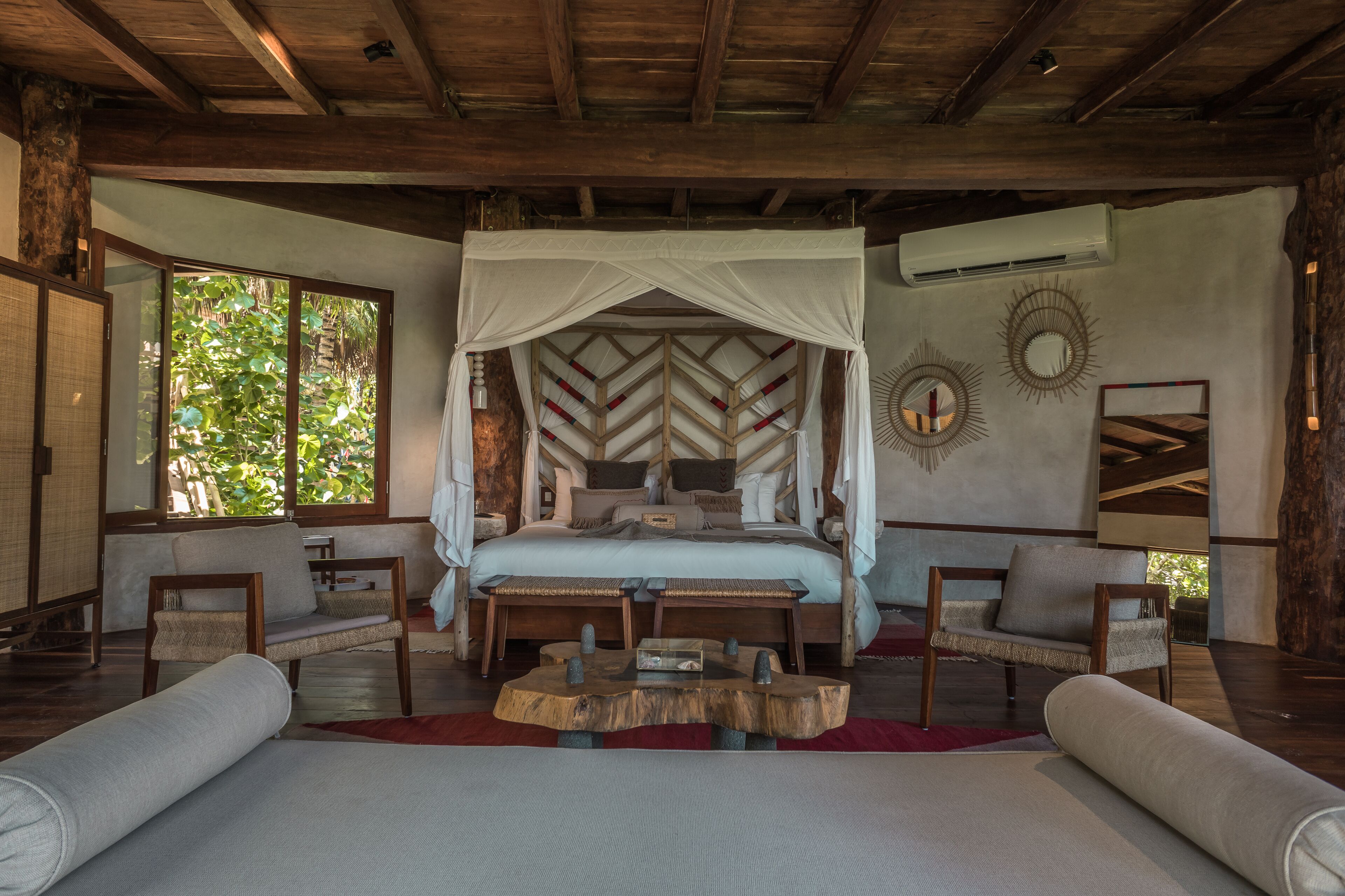 A spacious bedroom with a large bed, a wooden headboard, and a canopy. There are two chairs and a small table in the room.