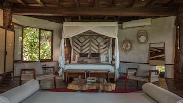 A spacious bedroom with a large bed, a wooden headboard, and a canopy. There are two chairs and a small table in the room.