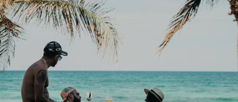 A poolside scene with palm trees, a clear sky, and people relaxing in the water.