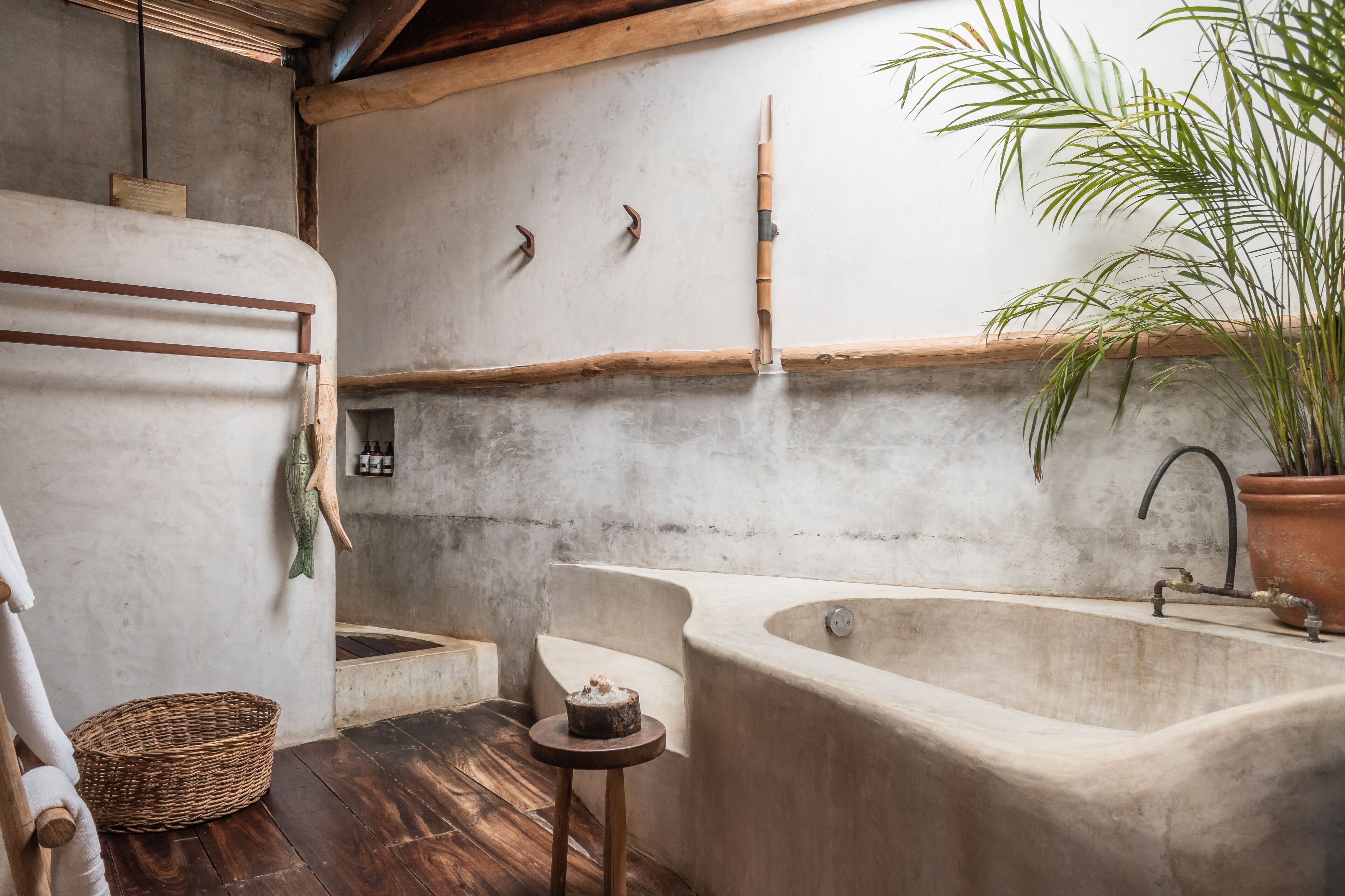 A rustic bathroom with a large bathtub, wooden beams, a potted plant, and a woven basket.