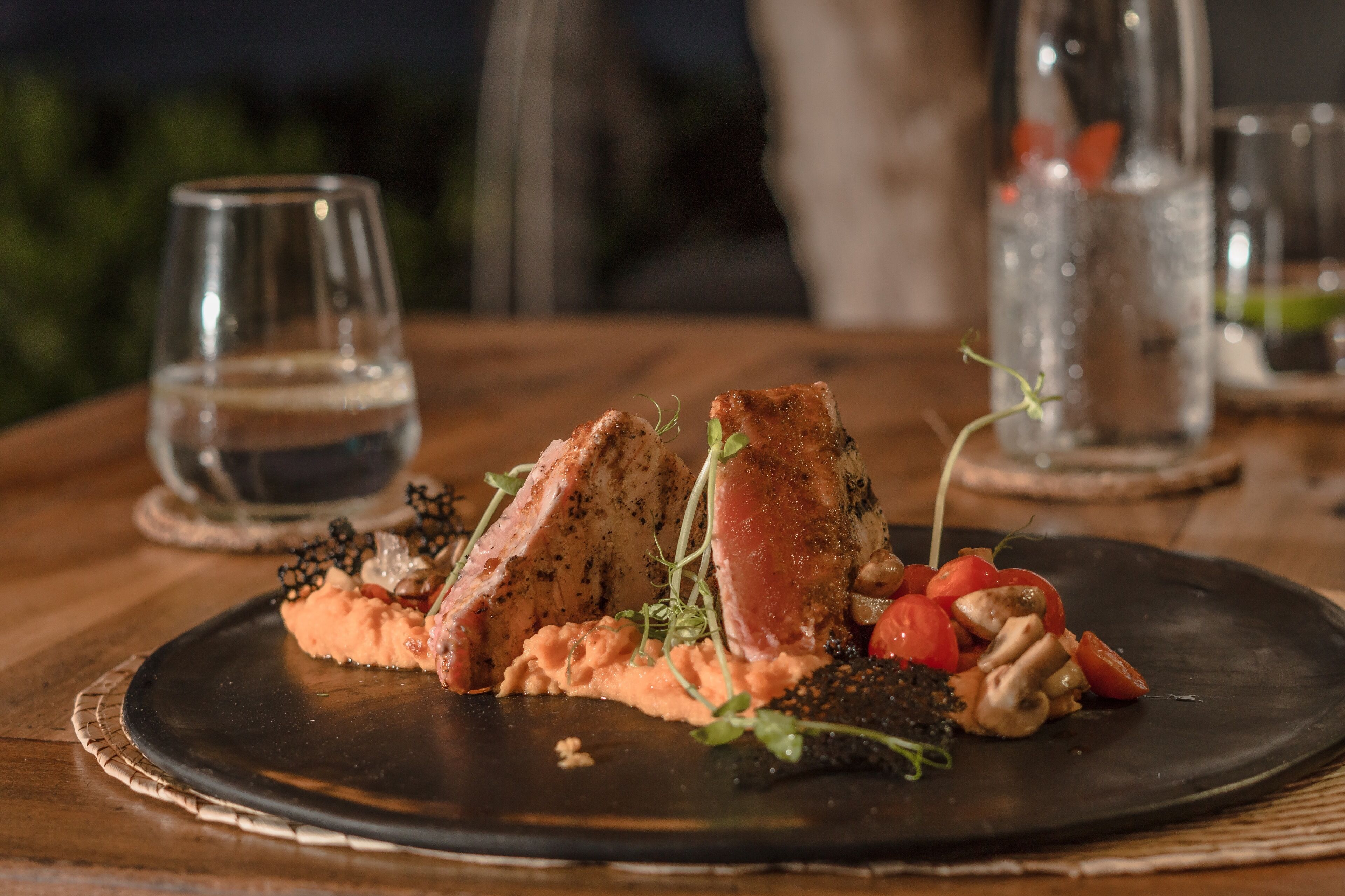 A plate of food with salmon, mushrooms, and cherry tomatoes, accompanied by a glass of water.