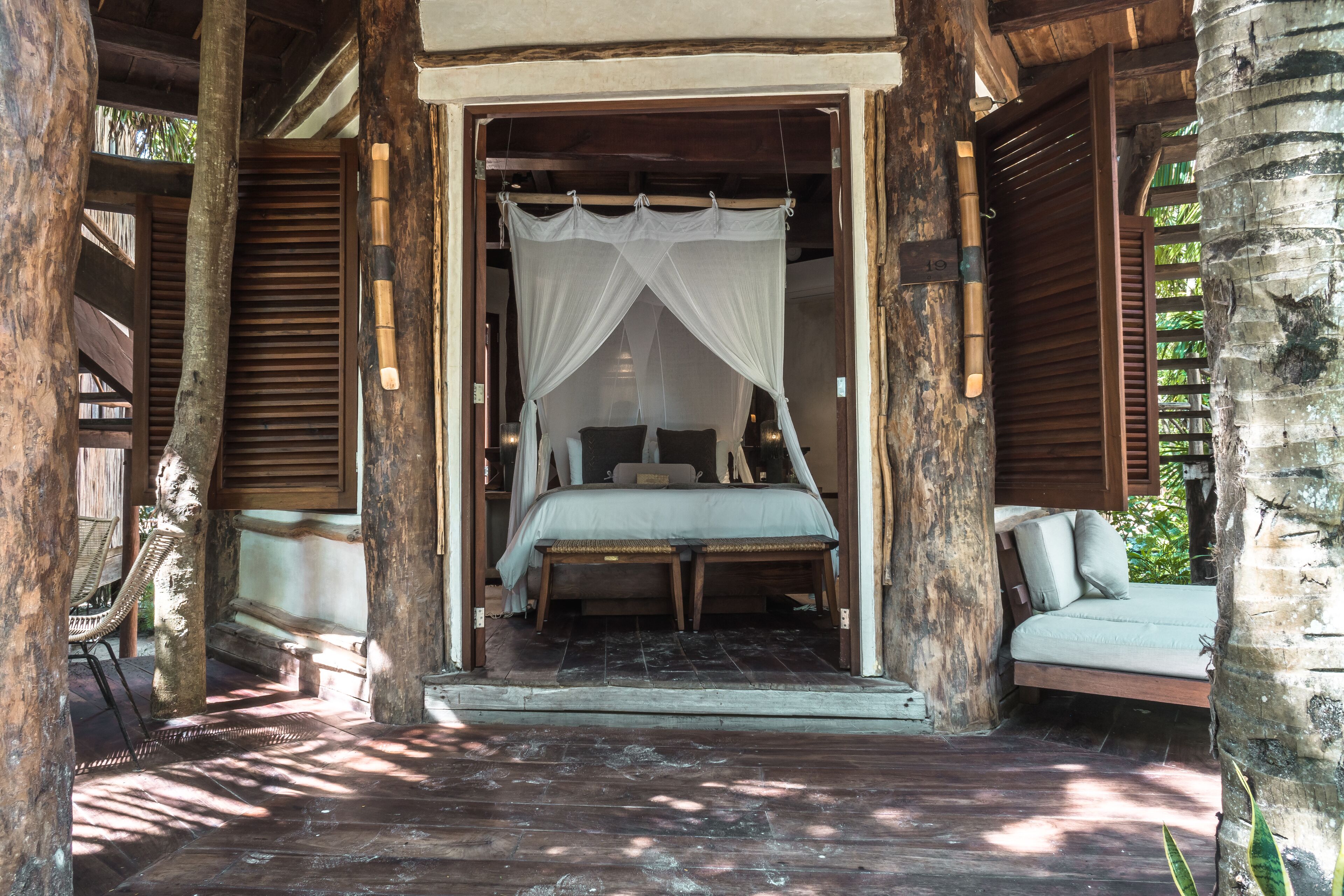 A bed with a canopy in a wooden structure with a bench and a tree nearby.