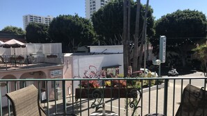 A balcony with wicker chairs and a small table, overlooking a street with a motel sign and buildings in the background. - Sea Shore Motel (Santa Monica)