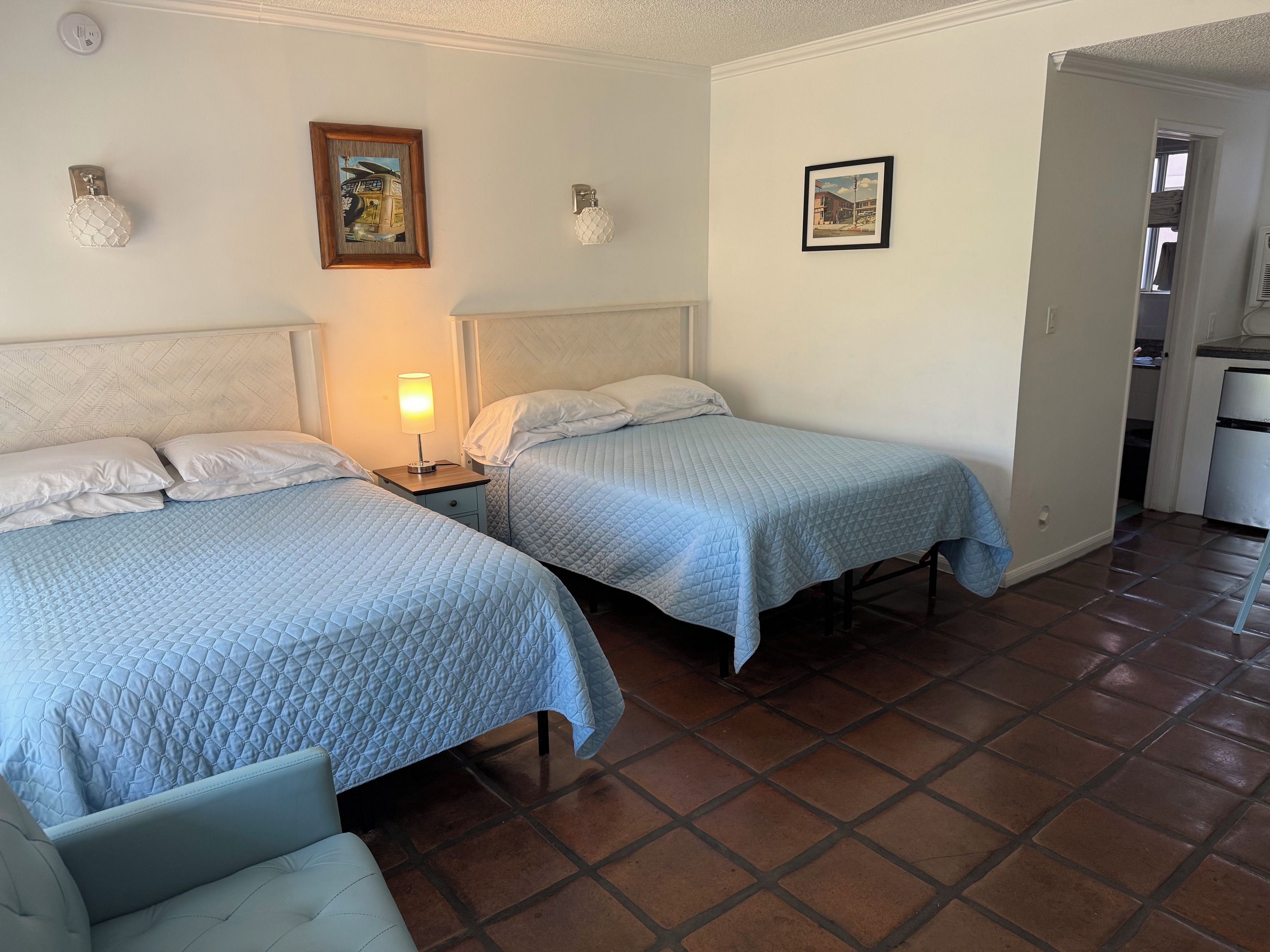 Een hotelkamer met twee bedden, een nachtkastje met een lamp en een kleine keukenunit.