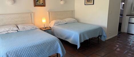 Een hotelkamer met twee bedden, een nachtkastje met een lamp en een kleine keukenunit.
