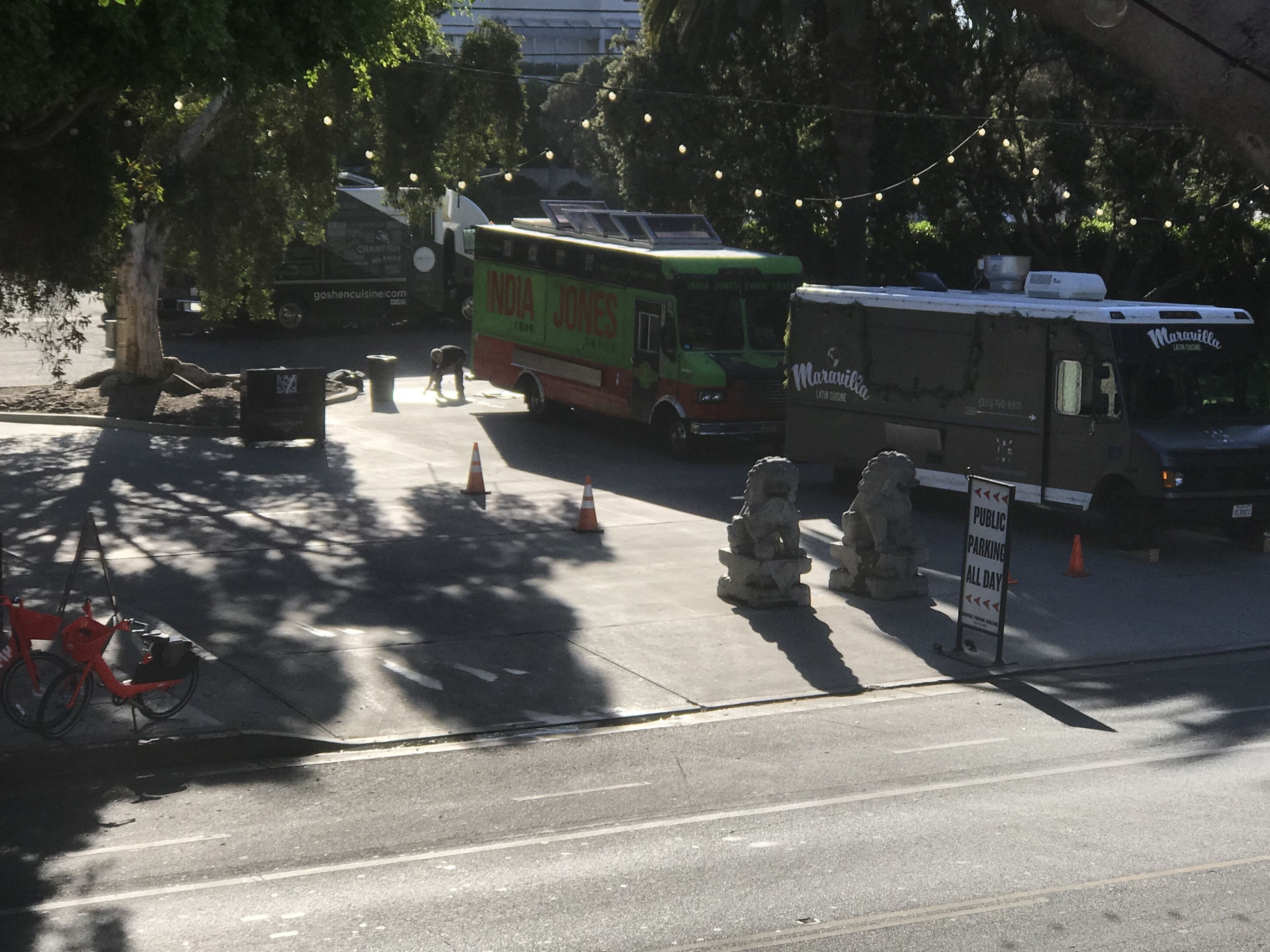 A street with a parked food truck and a delivery truck. There are traffic cones and a sign indicating public parking.