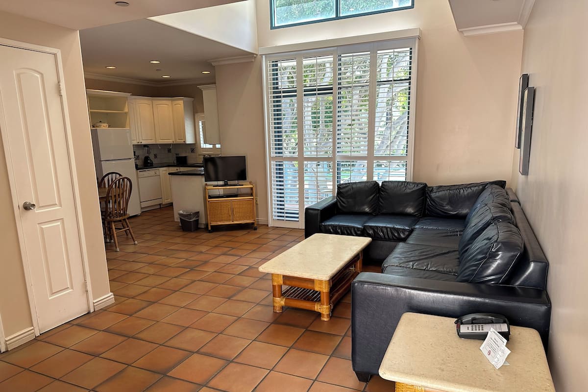 A living room with a black leather sofa, a wooden coffee table, and a television on a stand.