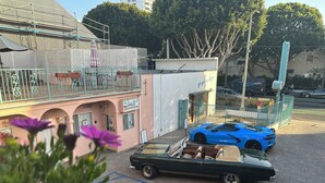 A pink building with a registration sign, a blue sports car, and a convertible on a trailer. - Sea Shore Motel (Santa Monica)