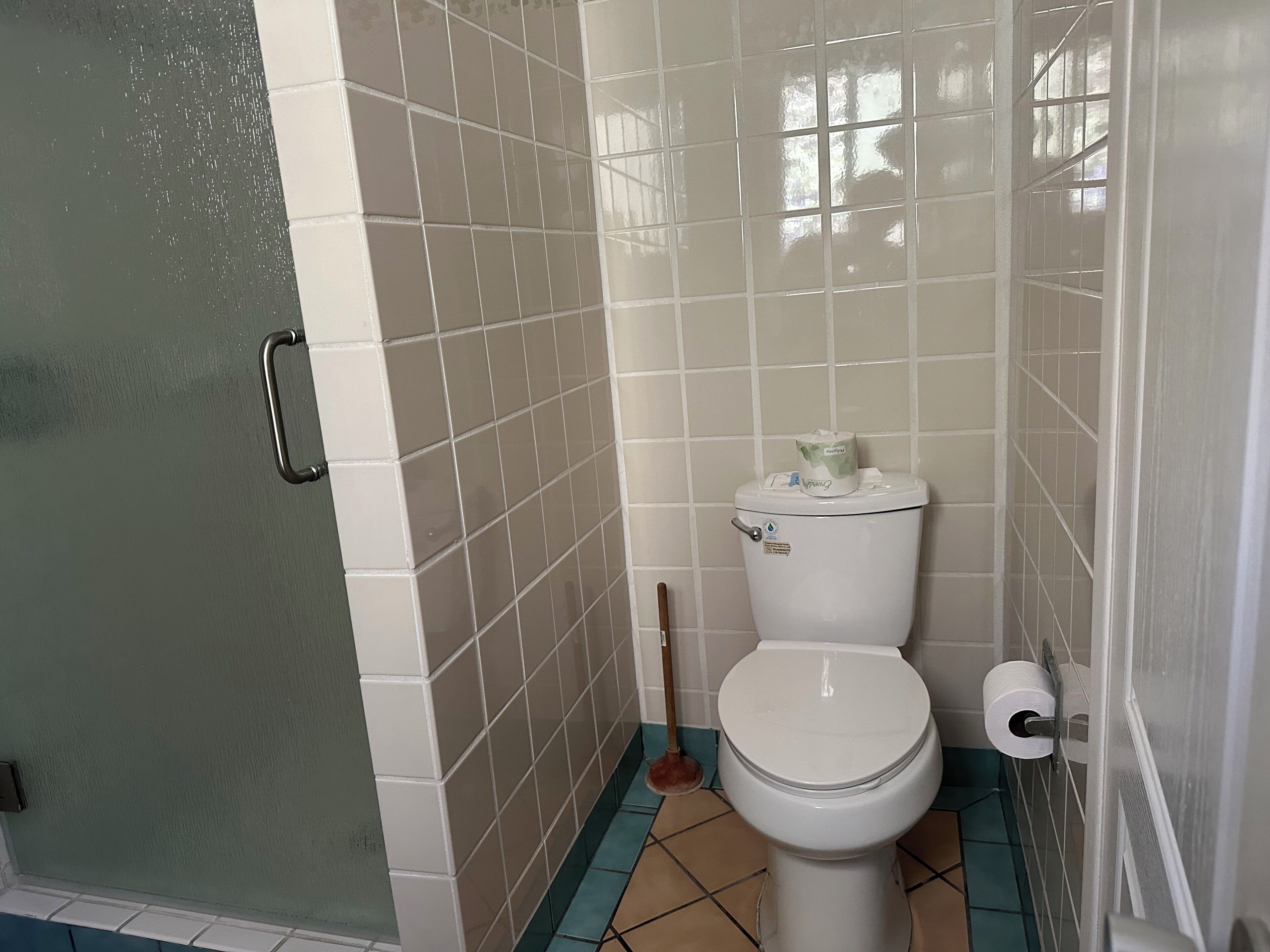 A bathroom with white tiled walls, a white toilet, and a blue and beige floor.