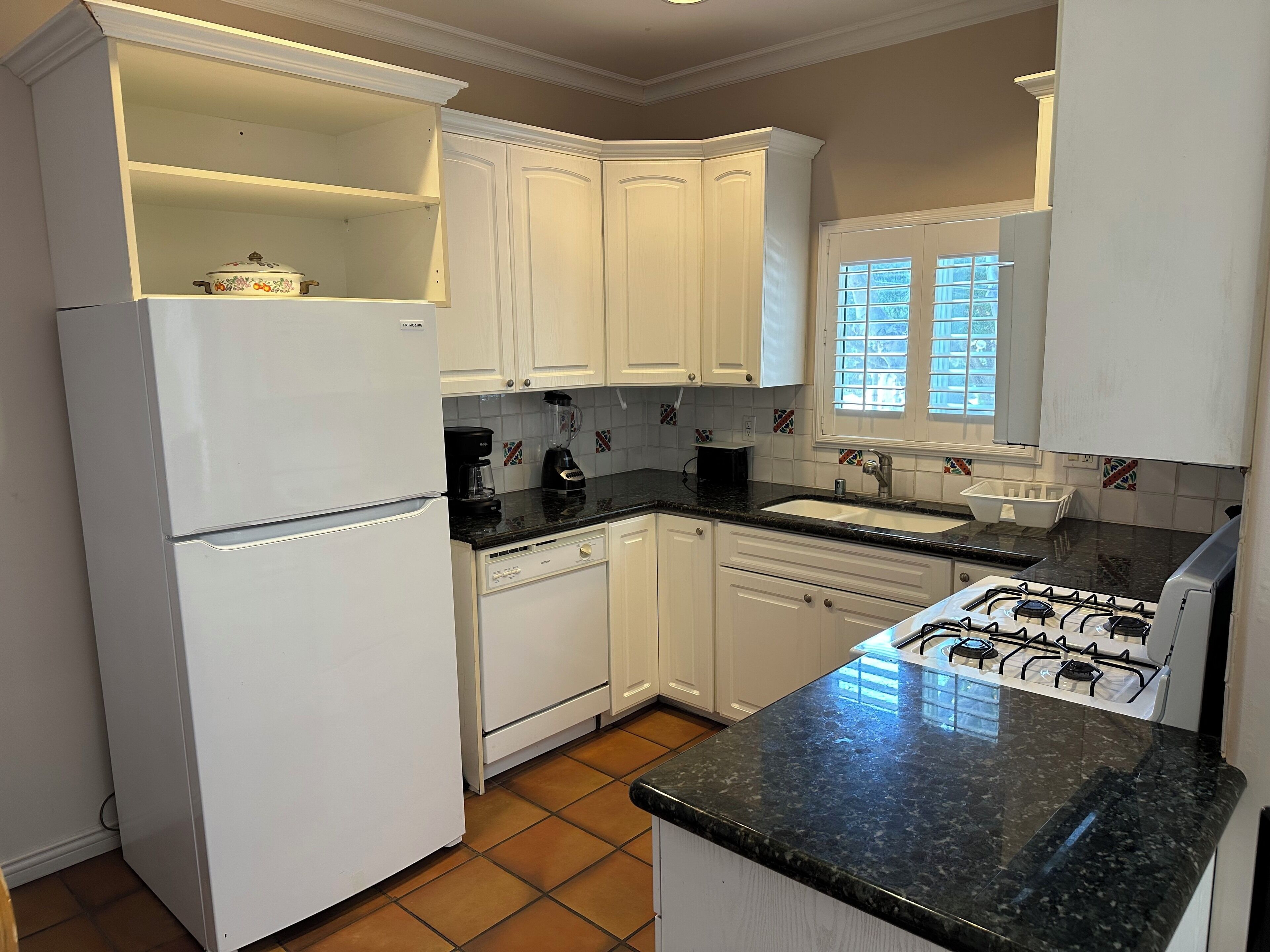 A kitchen with white cabinets, a black countertop, a stove, and a refrigerator.