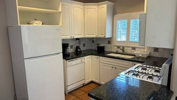A kitchen with white cabinets, a black countertop, a stove, and a refrigerator.
